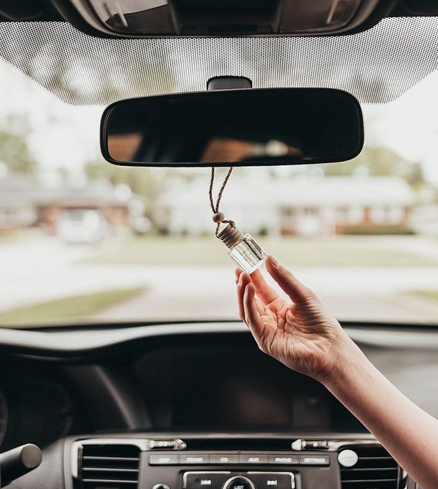 hand holds small glass container with rope around the rear view mirror 
