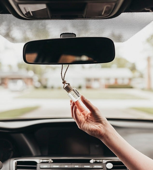hand holds small glass container with rope around the rear view mirror 