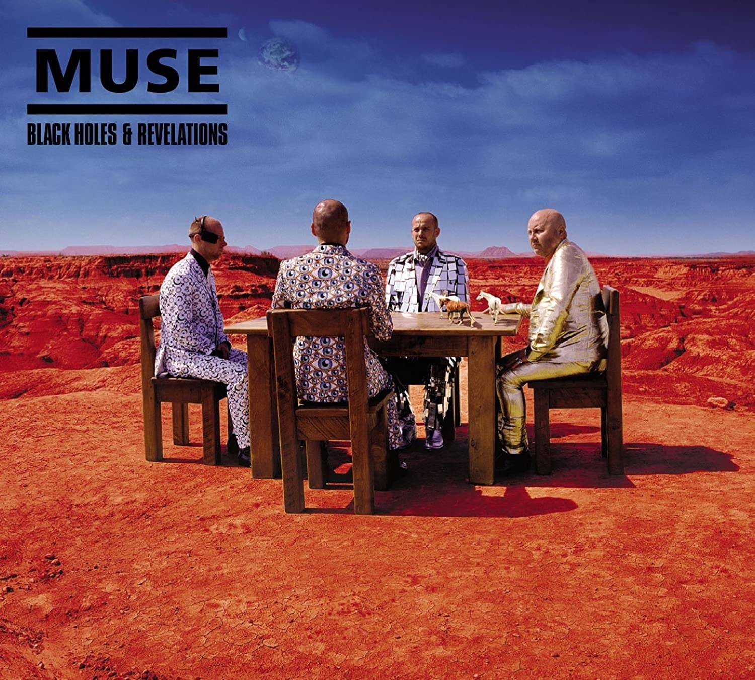 Men in suits, sitting at a wooden table, in the desert. 