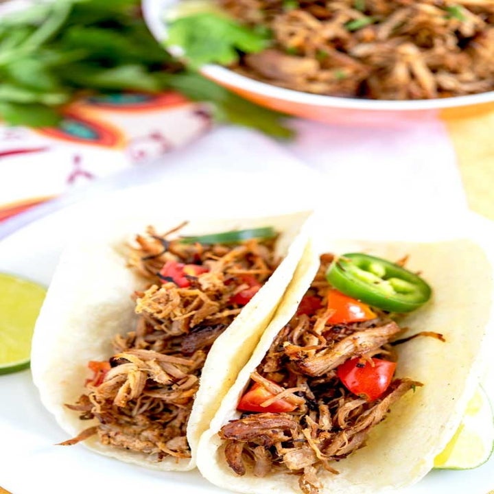 Two carnitas tacos topped with tomato and jalapeño.