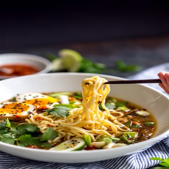 Chopsticks pulling noodles from a bowl of loaded ramen soup.