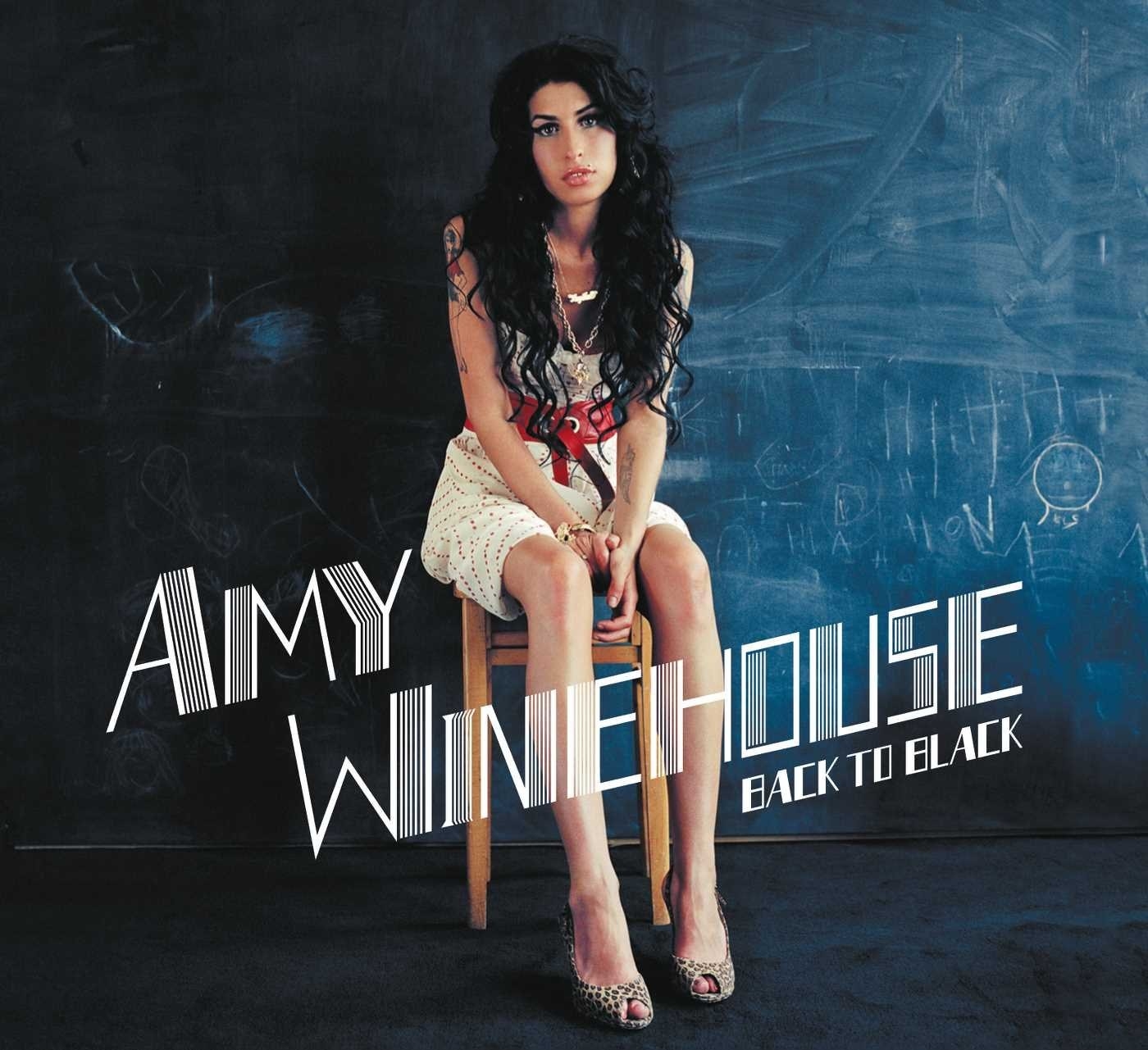 Amy Winehouse sitting on a stool in front of a chalkboard. 
