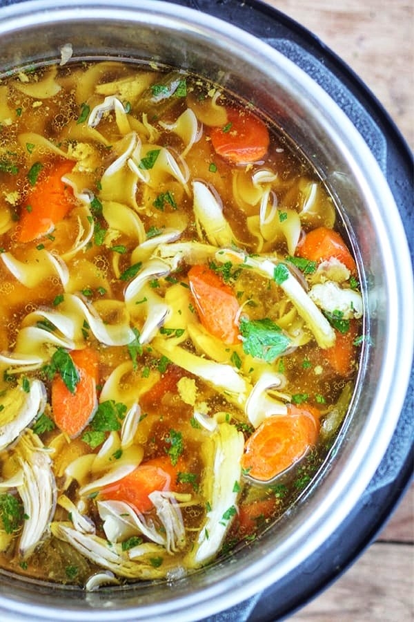 An Instant Pot filled with shredded chicken, egg noodles, diced carrots, and parsley in broth.