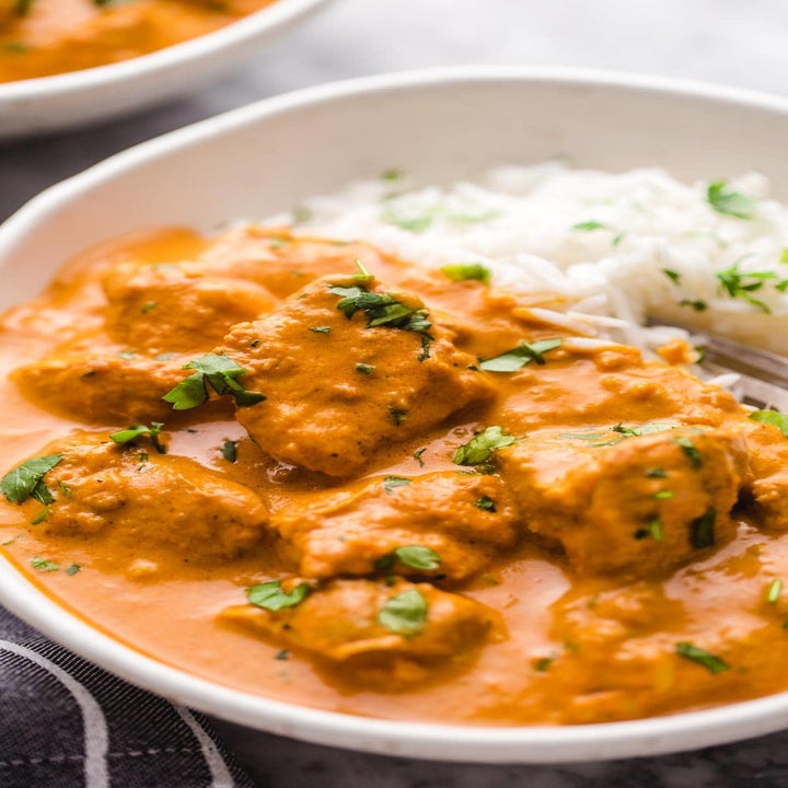 A bowl of Indian butter chicken with basmati rice on the side.