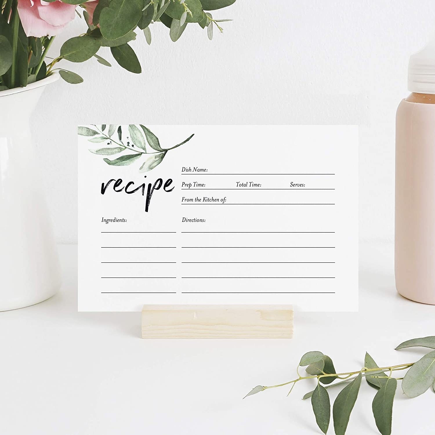 A recipe card on a holder next to a plant and a water bottle