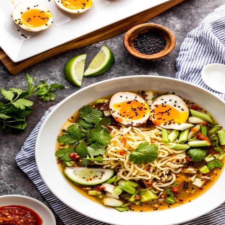 A bowl of ramen chicken soup with soft boiled egg, green veggies, and fresh herbs.
