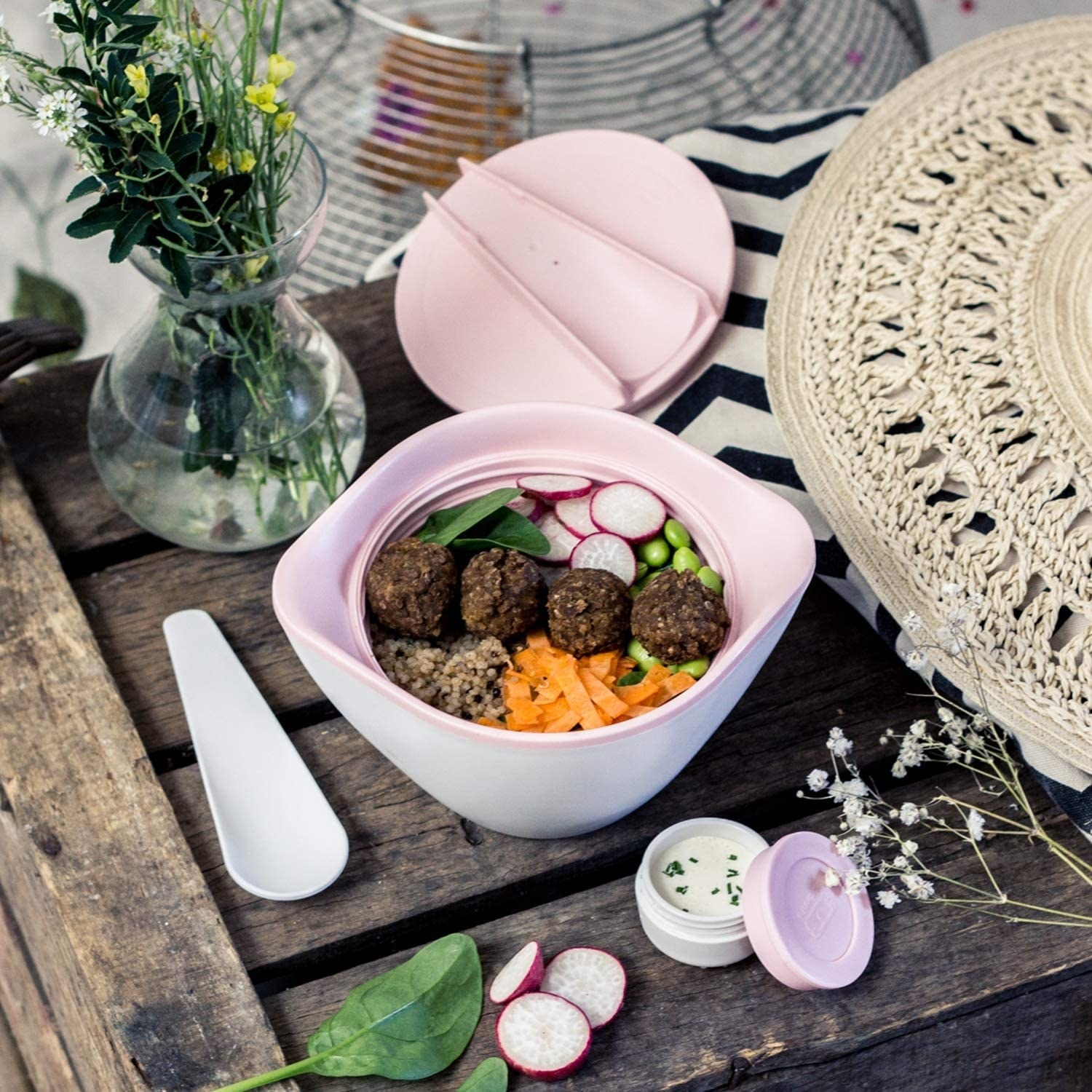 The bowl filled with a salad next to a vase of flowers