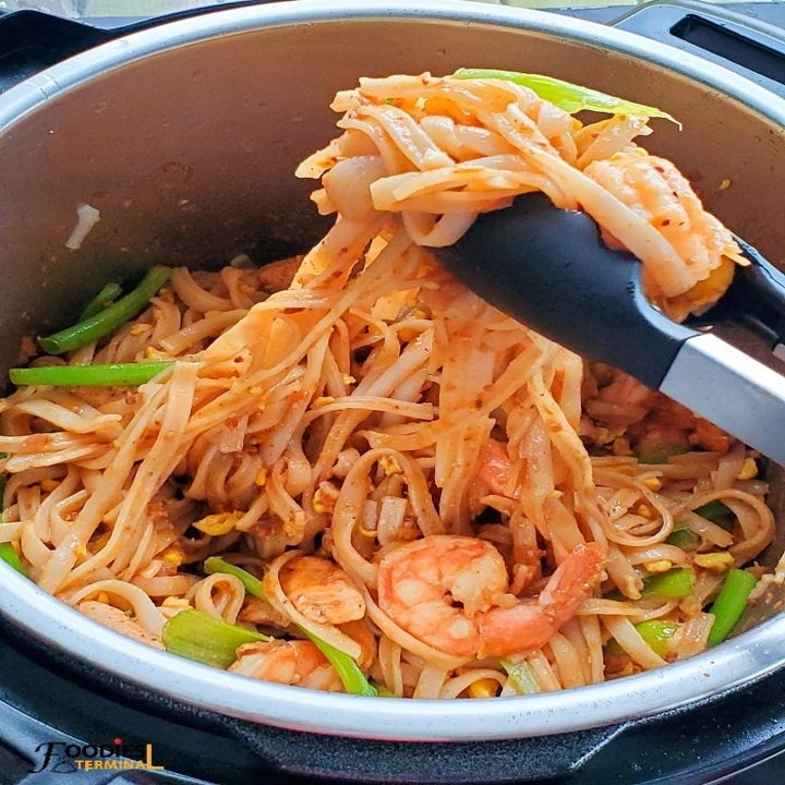 Tongs pulling a portion of pad Thai with shrimp out of an Instant Pot.