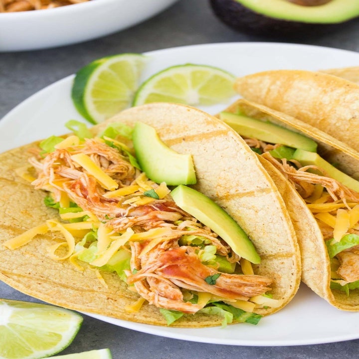 Two shredded chicken tacos with lettuce, cheese, tomato, and avocado.