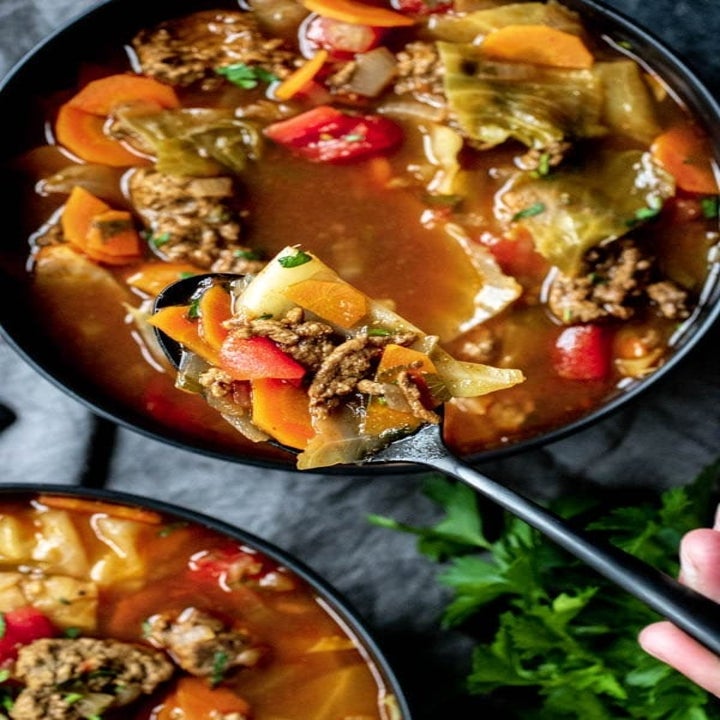 Two bowls of cabbage soup with beef and carrots in a tomato-based broth.