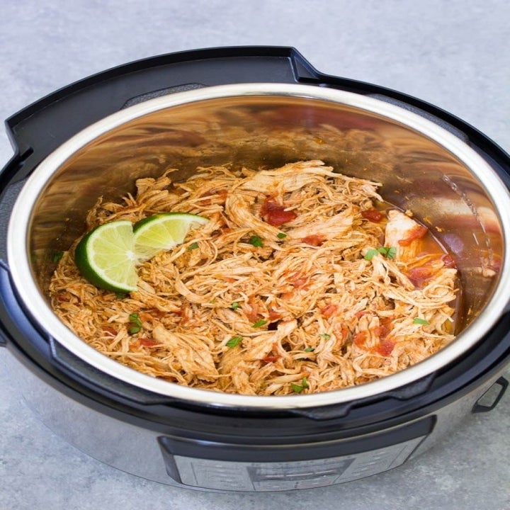 An Instant Pot filled with shredded chicken in a tomato sauce with lime wedges.