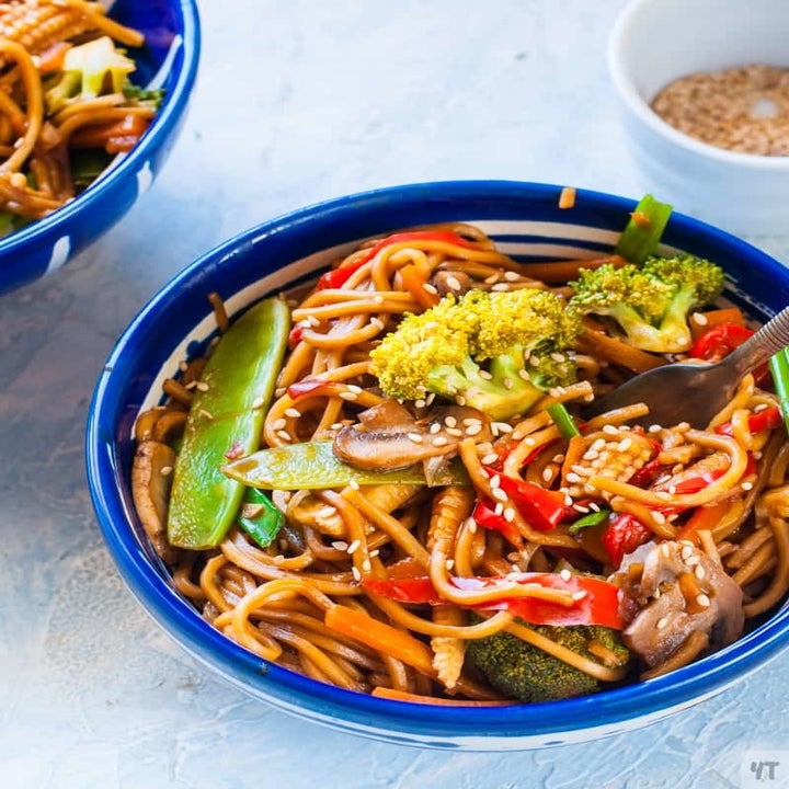 A bowl of lo mein noodles stir fried with colorful veggies and topped with sesame seeds.