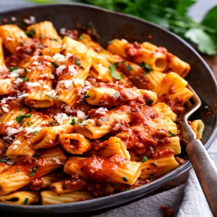 A big bowl of penne tossed in Bolognese sauce with grated cheese on top.