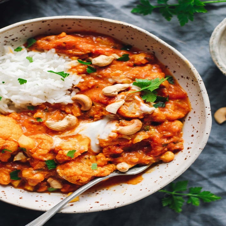 Cauliflower tikka masala topped with cashews, yogurt, fresh herbs, and a side of rice.