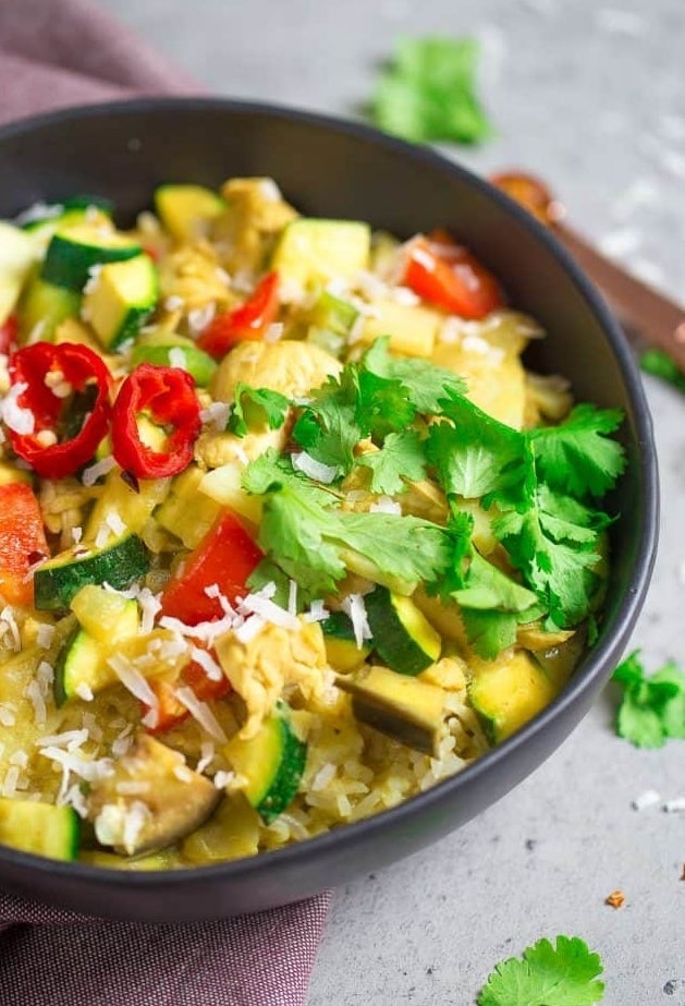 A bowl of Vegetable green curry with zucchini, peppers, and squash over rice with cilantro.