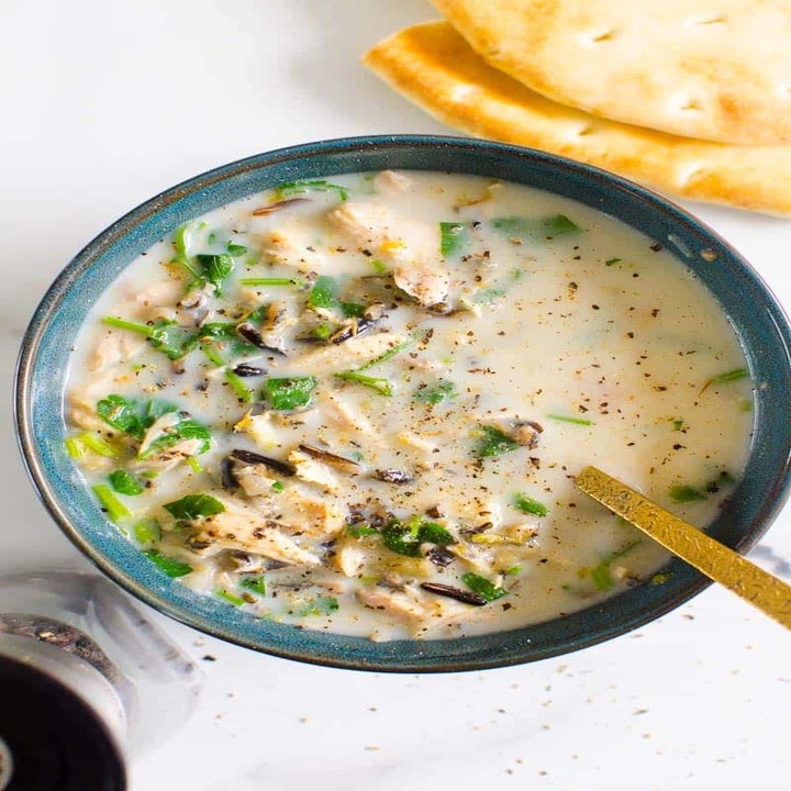 A bowl of creamy soup with pieces of chicken, wild rice, and fresh herbs.