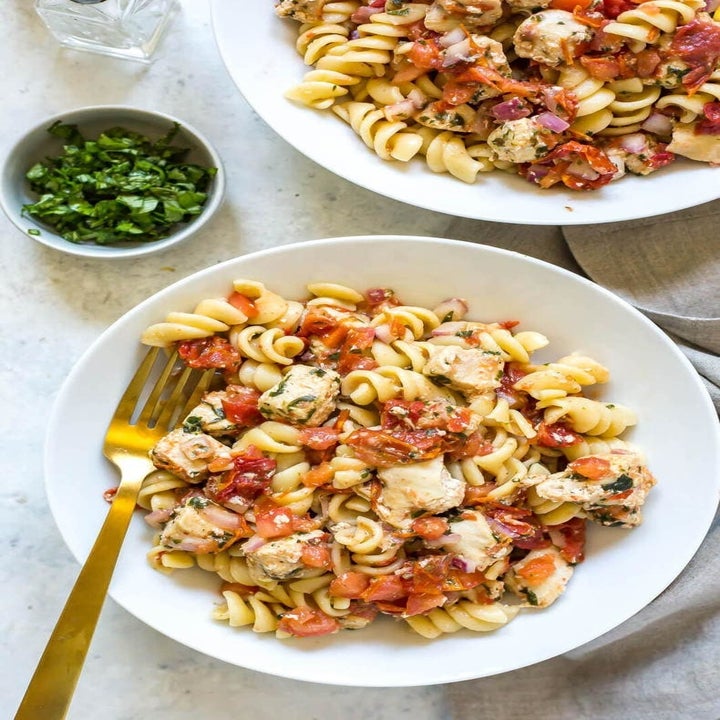 Two bowls of bruschetta chicken pasta with fresh basil in a bowl to the side.