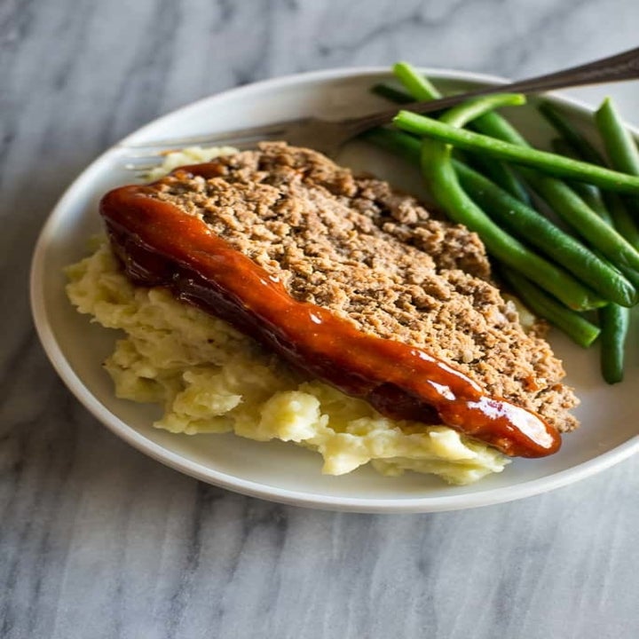 A plate of meatloaf over mashed potatoes with a side of green beans.