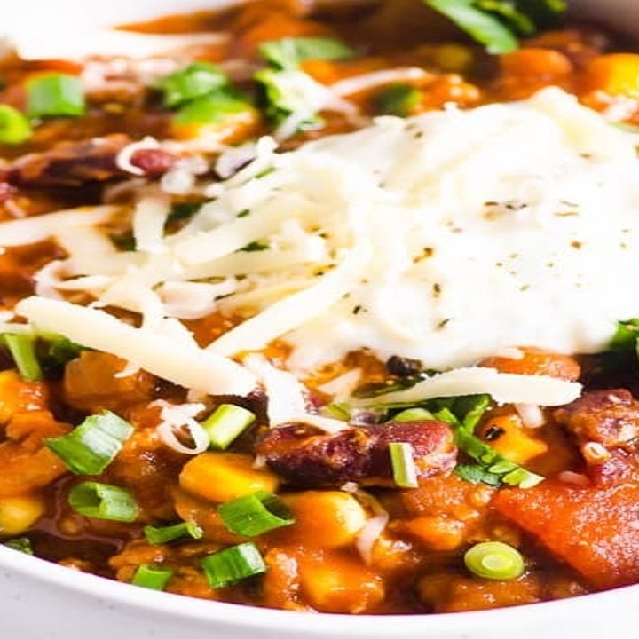 A bowl of turkey chili topped with shredded cheese and scallions.