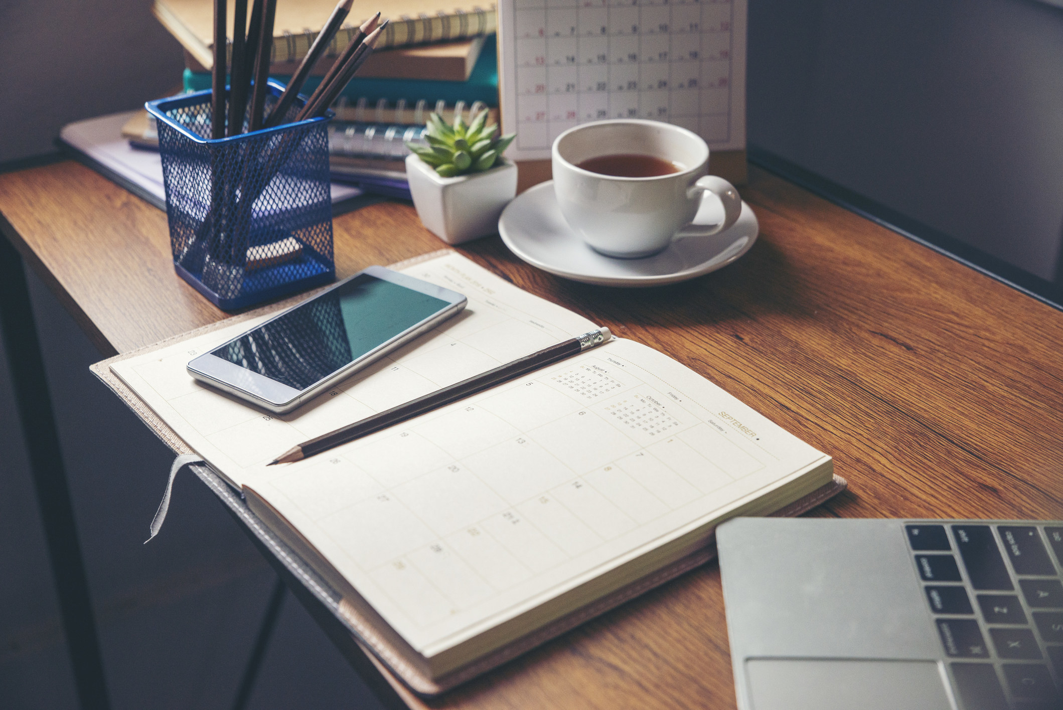 A desk with an open calendar and cell phone set on top of it.