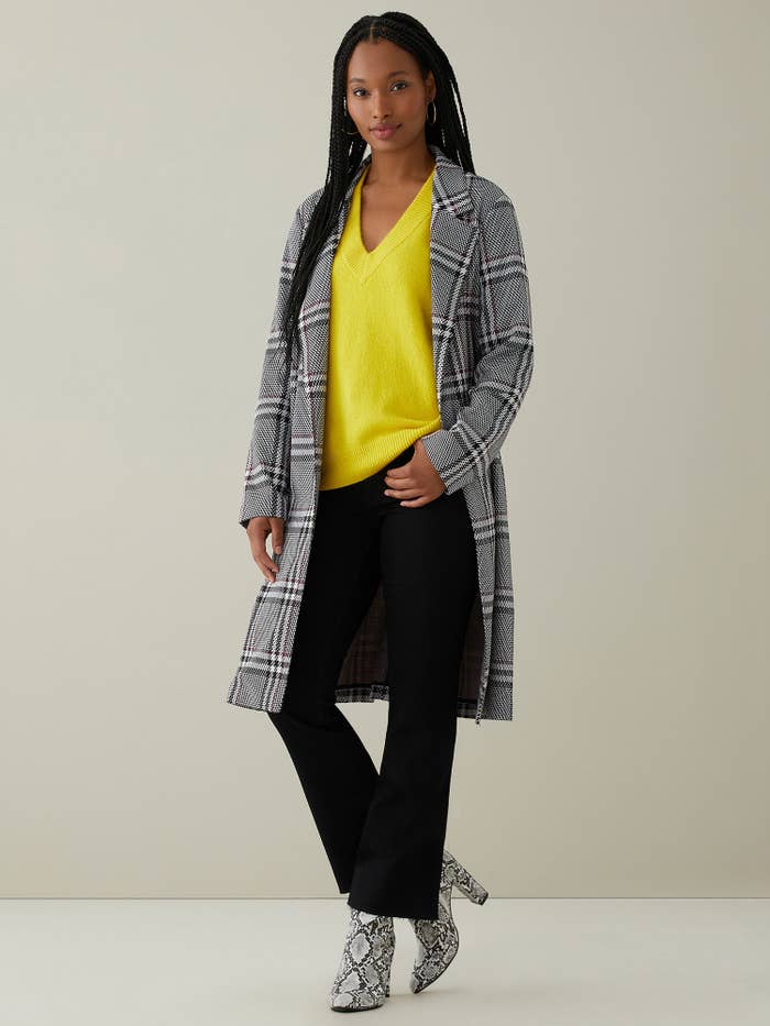 person wearing a gray coat over a yellow sweater and black pants
