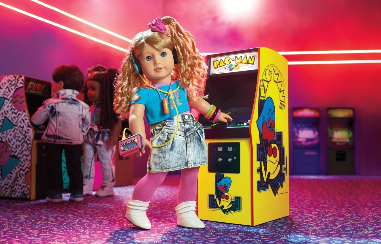 Courtney in a jean skirt and crop top and scrunchie at an arcade playing PAC-MAN