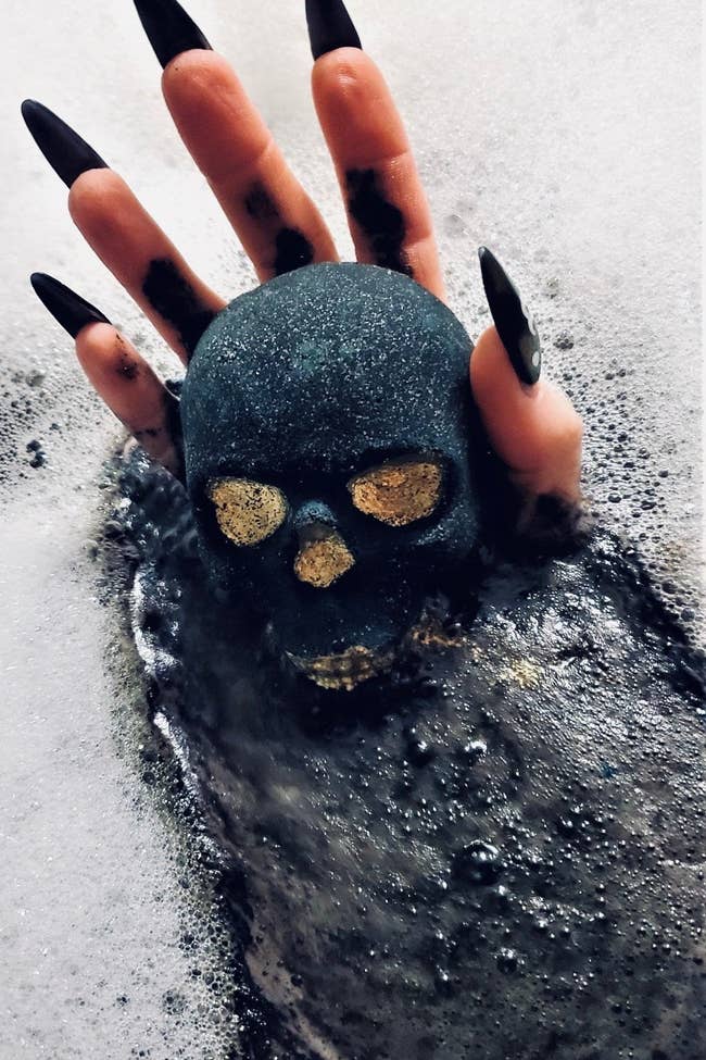 Hand with long fingernails holding skull bath bomb in bubble bath
