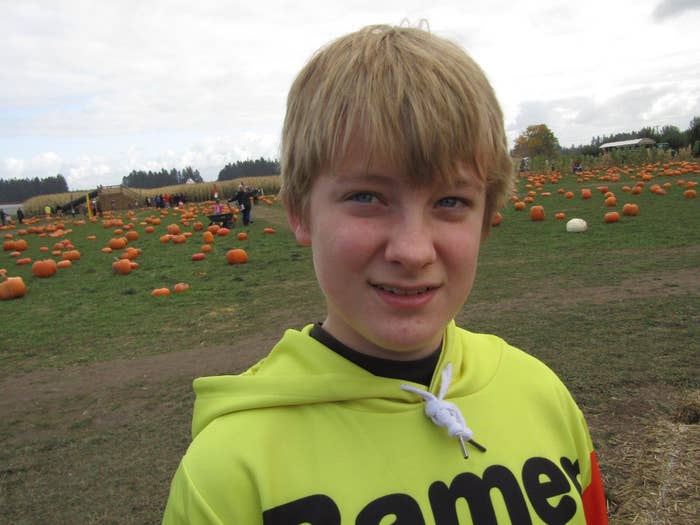 A young boy smiles at the camera in a pumpkin patch