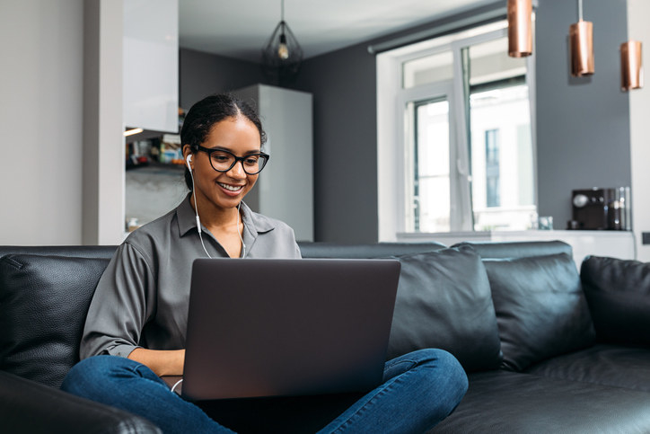 Young woman using a laptop sitting on a sofa wearing earphones