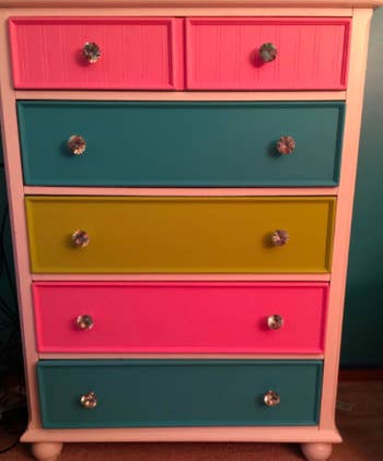 Reviewer shows white crystal dresser knobs on dresser with pink, blue, and green drawers 