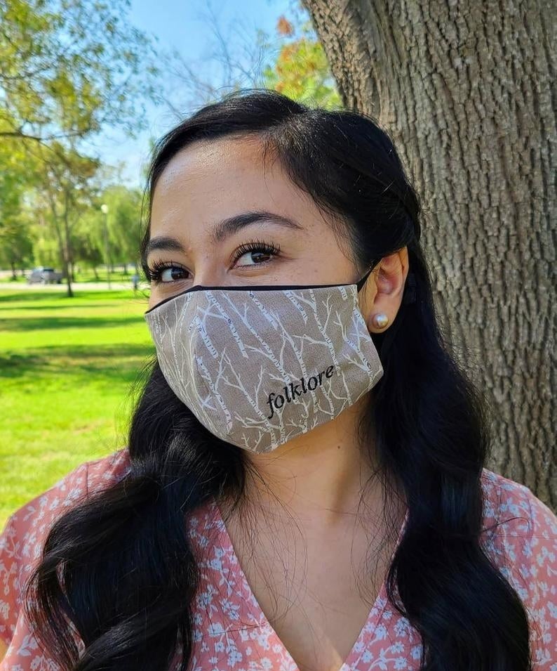 Model in beige tree print mask that says folklore on the bottom right side