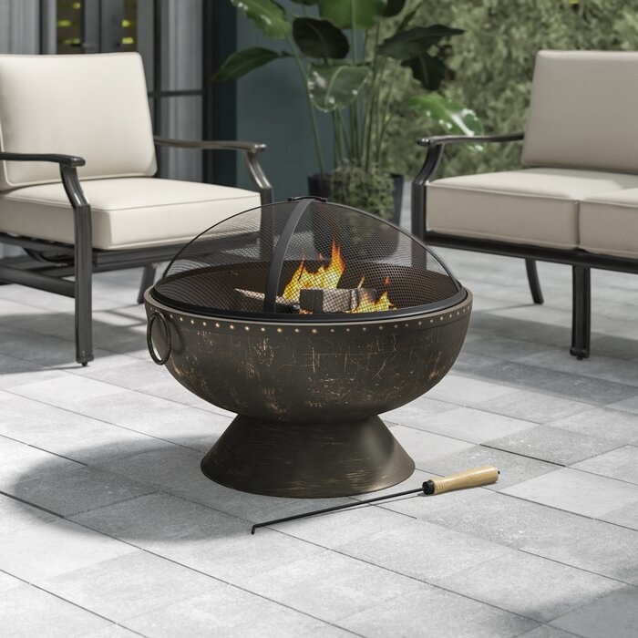 A stainless steel fire pit, lit on a patio.