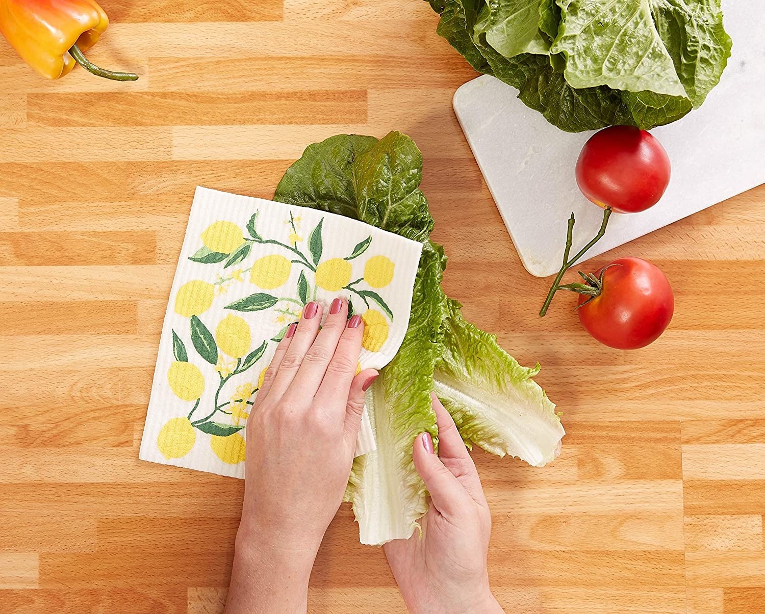 Close up of a model's hands using the dishcloth with a lemon illustration to clean some lettuce.