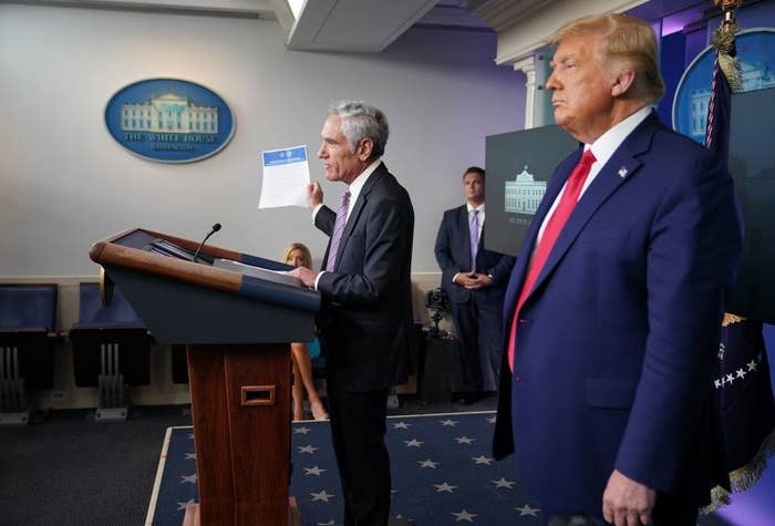 Trump stands behind Atlas, who speaks at a lectern and holds up a document