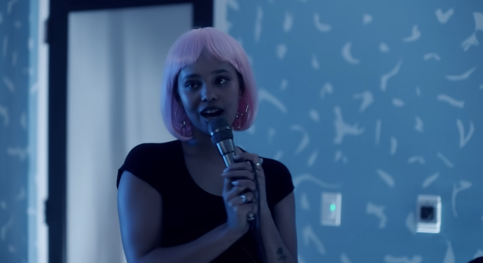 Alisha, in a pink wig, singing karaoke. 