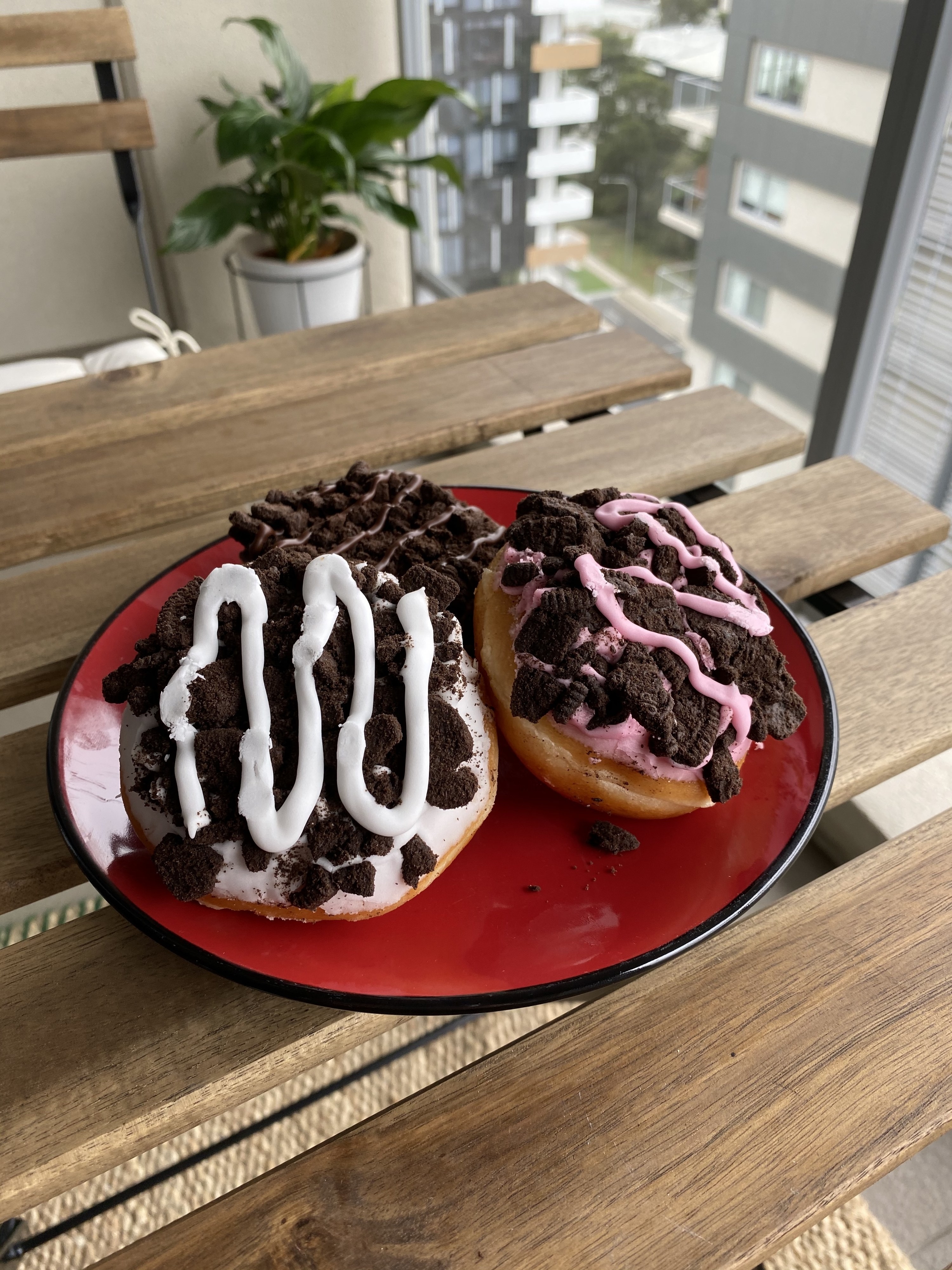 Three doughnuts sitting on a plate, one with strawberry icing, another with chocolate and the last with white icing