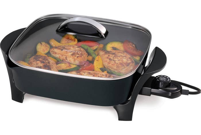 a black electric skillet cooking meat and vegetables