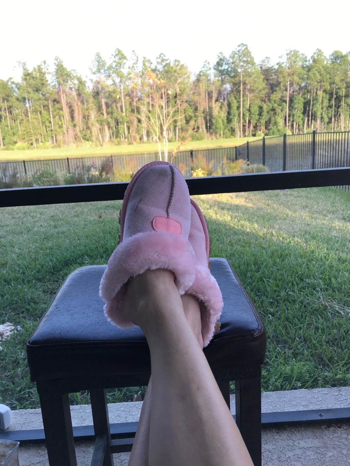 Someone wearing pink faux-fur suede slippers outdoors.