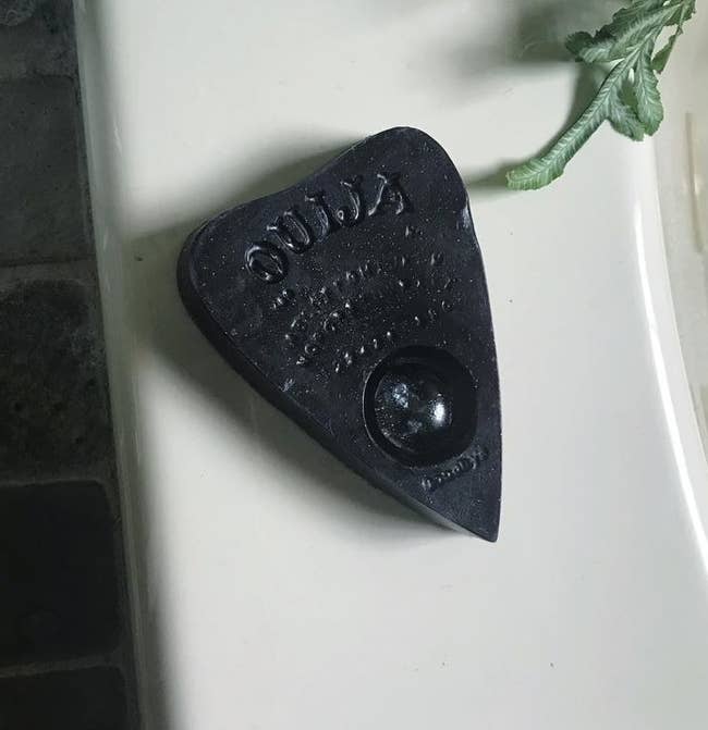 Planchette shaped soap in style of ouija board on bathtub edge