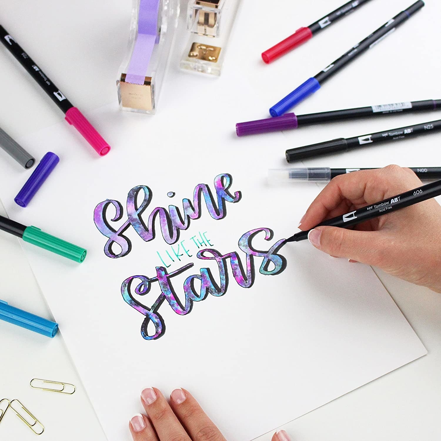 A person writing &quot;shine like the stars&quot; with a brush pen