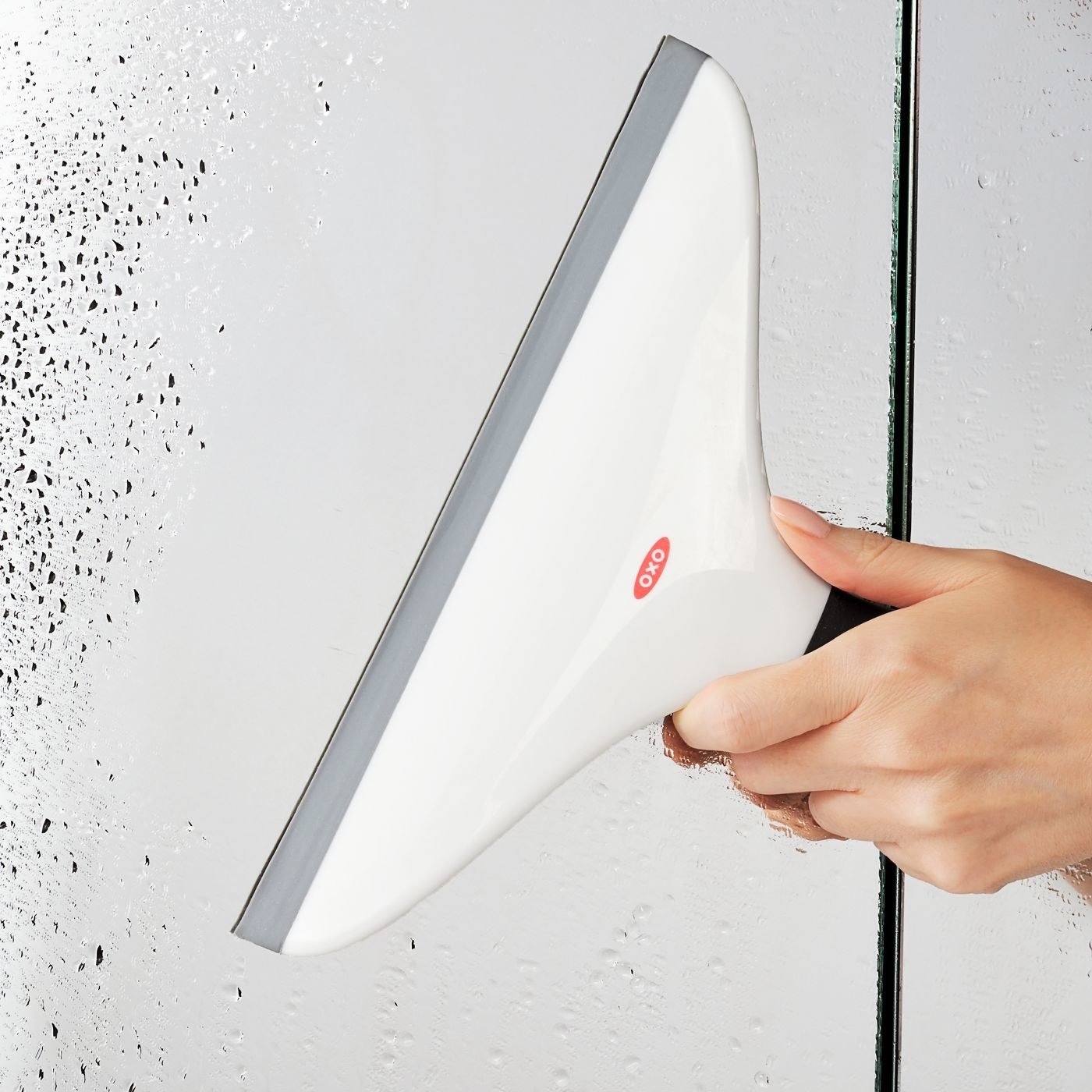person using white squeegee to clean shower door