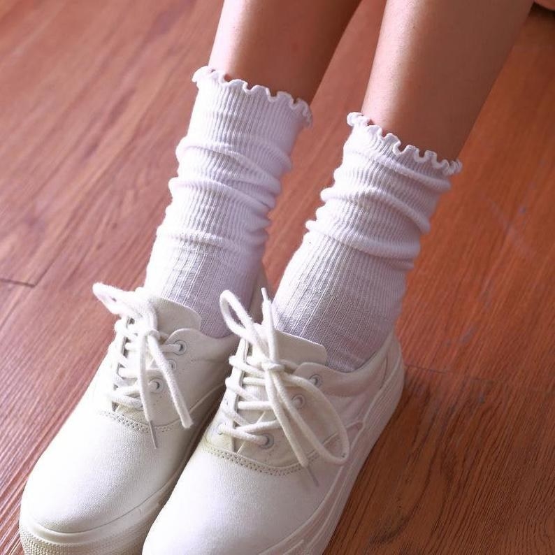 A photo of a kid and her white canvas shoes wearing white ribbed ruffled socks