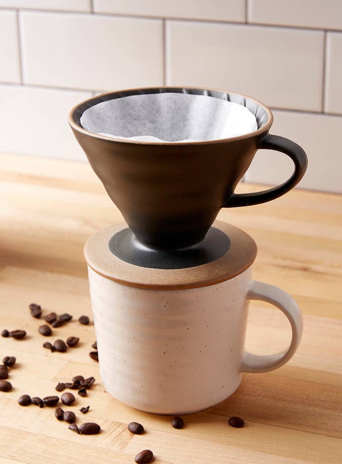 A stoneware pour over coffee dripper with a handle placed on top of a small mug