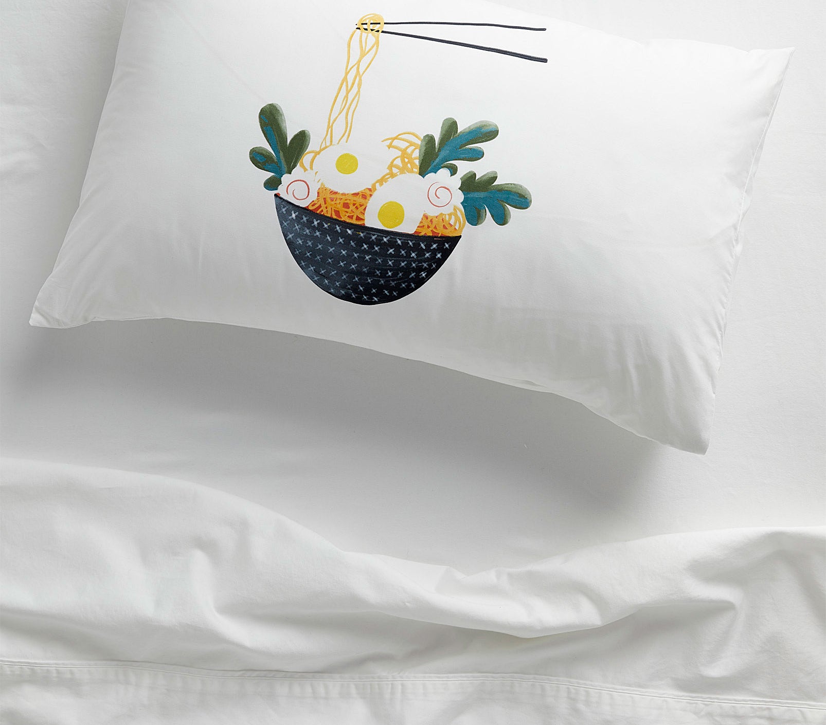 A bed with a large pillow that has a pillowcase with a drawing of a bowl of ramen on it