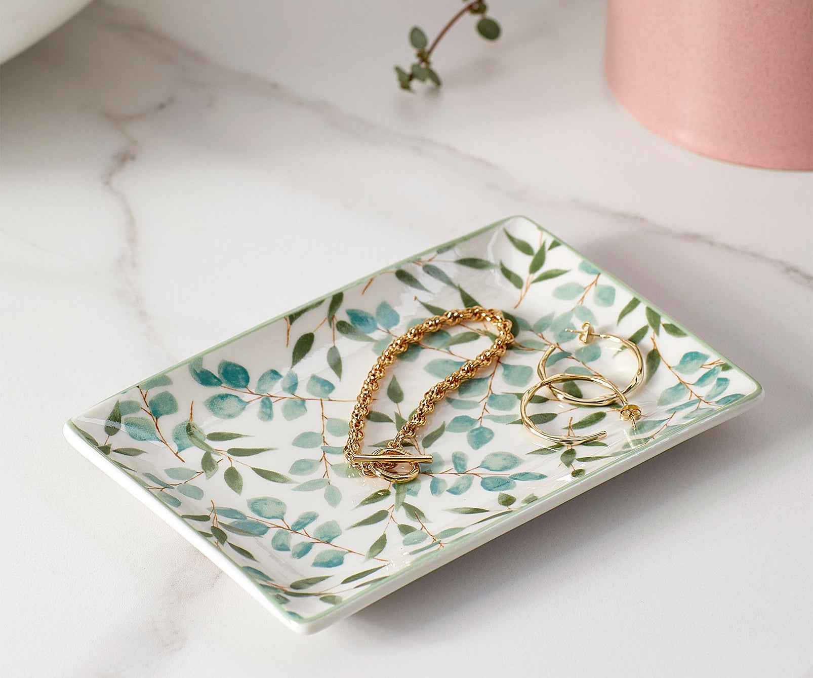A small ceramic tray with a gold bracelet and pair of earrings on it