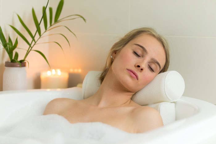 Person resting head and shoulders on mid-century-modern style bath pillow while soaking in bubble bath