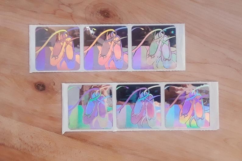 Six iridescent SandyLion ballet slipper stickers still on the sticker strip 