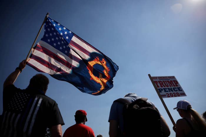 QAnon supporters waving an American flag emblazoned with a &quot;Q&quot; and a Trump/Pence 2020 sign