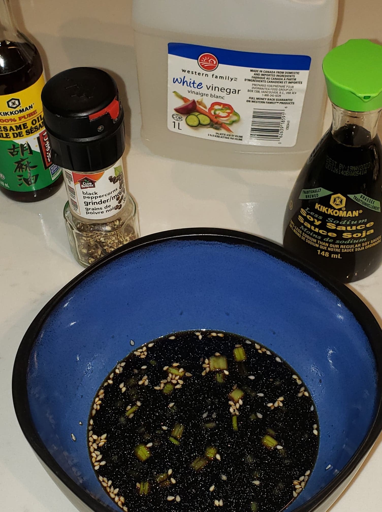 A bowl of the finished dipping sauce next to bottles of sesame oil, soy sauce, black pepper, and white vinegar