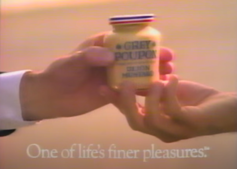 A screenshot of one hand handing another hand a jar of Grey Poupon with &quot;One of life&#x27;s finer pleasures&quot; written underneath it from the commercial for it